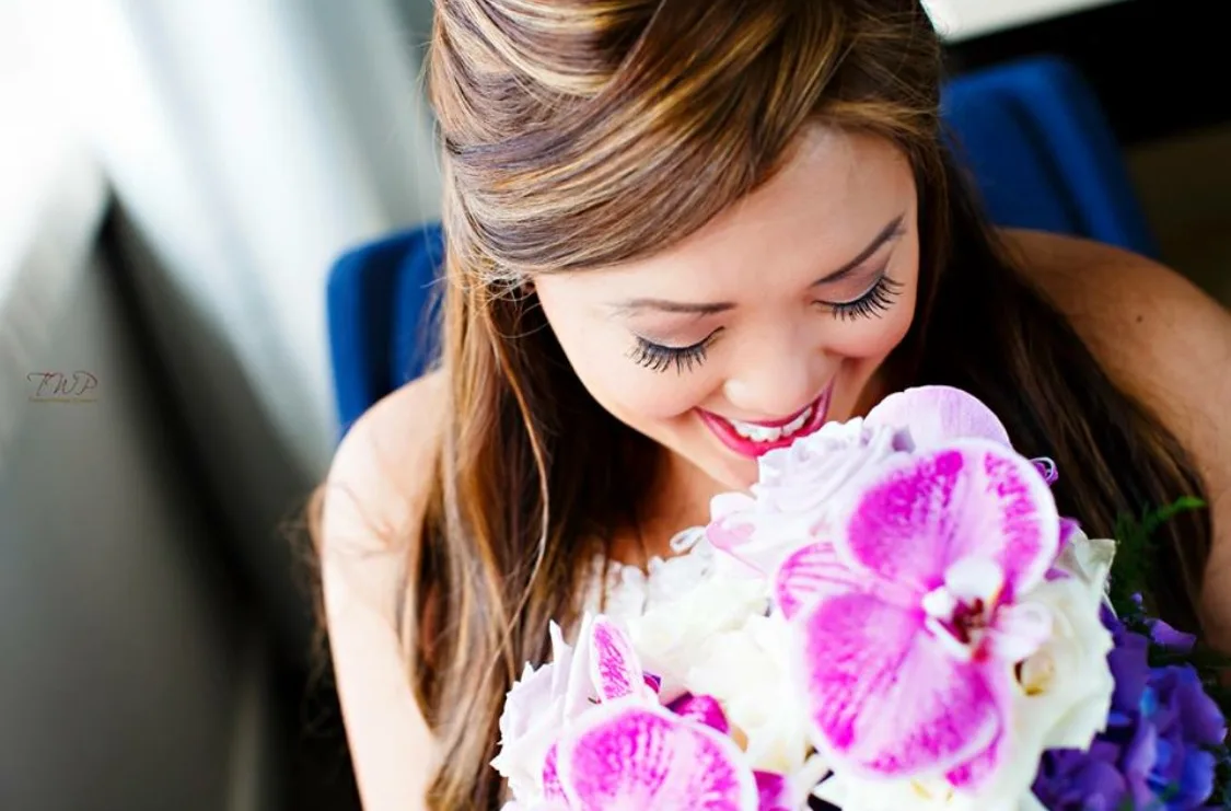Bride smiling into a bouquet of orchids with soft romantic makeup